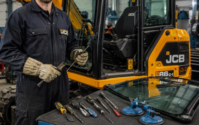 Technician wearing safety glasses gloves and protective clothing for JCB cab glass replacement