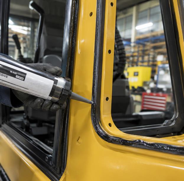 Applying polyurethane adhesive bead to JCB excavator cab frame before glass installation